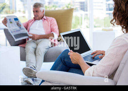 Woman using laptop while man reading newspaper Stock Photo