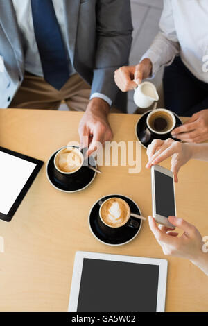 Colleagues having a cup of coffee while using mobile phone and digital tablet Stock Photo