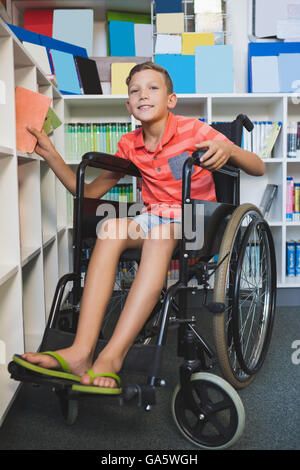 Disabled schoolboy selecting a book from bookshelf in library Stock Photo