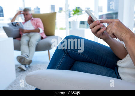 Midsection of woman using mobile phone while man reading newspaper Stock Photo