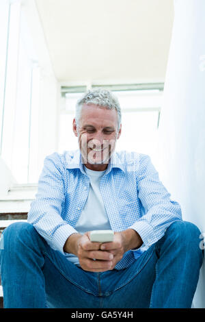 Smiling mature man using smartphone at home Stock Photo