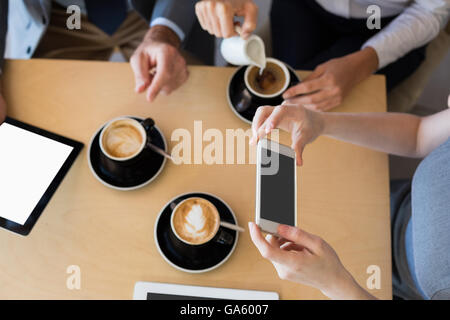 Colleagues having a cup of coffee while using mobile phone and digital tablet Stock Photo