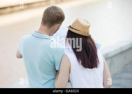 Beautiful young loving couple is looking at map. They are standing with their backs to the camera, searching the way Stock Photo