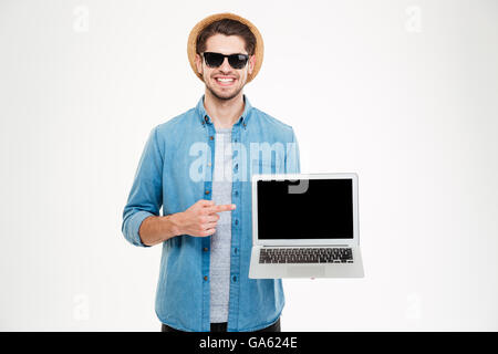 Happy confident young man in sunglasses and hat pointing on blank screen laptop Stock Photo