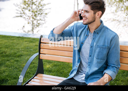 Handsome man sitting on the bench and talking on the phone outdoors Stock Photo