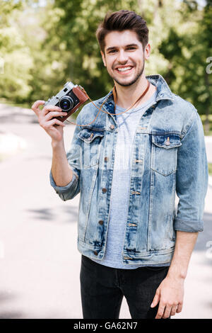 Portrait of a handsome hipster guy holding camera outdoors in the park Stock Photo