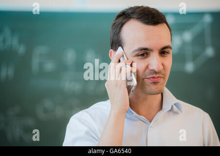 portrait closeup on a man talking phone at classroom in front of chalkboard Stock Photo