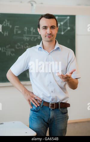 Young teacher near chalkboard in school classroom talking to class Stock Photo