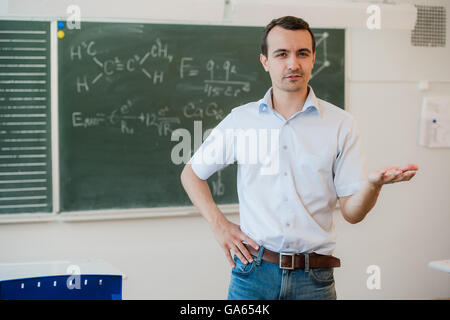 Young teacher near chalkboard in school classroom talking to class Stock Photo