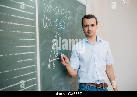 Young male teacher or student holding chalk writing on chalkboard in classroom Stock Photo