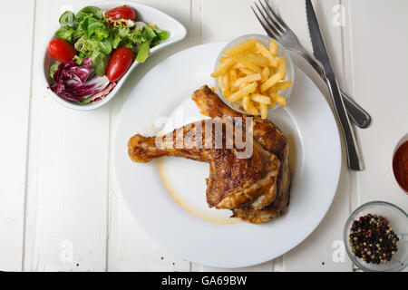Roast chicken thighs and fries, and salad of lettuce and tomato on white wooden table Stock Photo