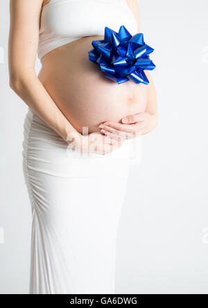 A pregnant woman cradels her baby belly with  gift bow attached. Stock Photo