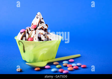 frozen yogurt with chocolate and chocolate candy topping on blue background with green spoon and chocolate candy Stock Photo