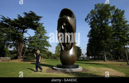 A Gardener walks past Henry Moore's sculpture called Large Upright Internal/External Form at Kew Gardens in London. Stock Photo