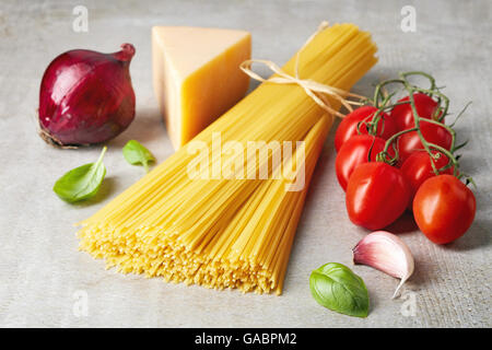 Spaghetti pasta, tomato, cheese, onion, garlic and basil leaves on grey stone table Stock Photo