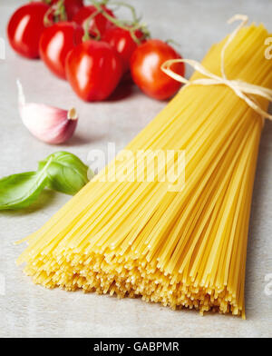 Spaghetti pasta, tomato, garlic and basil leaves on grey stone table Stock Photo