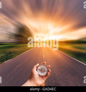 Hand man holding compass on blurred road with sky sunset. Stock Photo