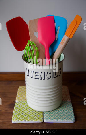 Retro kitchen utensils pot on wooden counter and tiles with six bright and colourful baking spatula whisk and spoons to cook Stock Photo