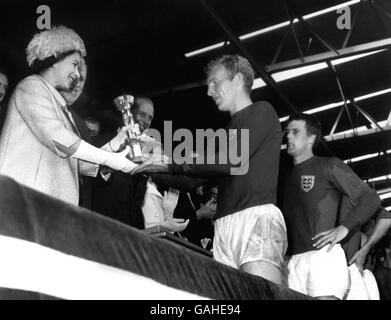 England v West Germany - 1966 World Cup Final - Wembley Stadium. England captain Bobby Moore is presented with the Jules Rimet trophy by Her Majesty The Queen as teammate Geoff Hurst (r) looks on in awe Stock Photo