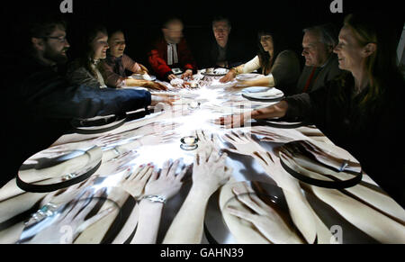 Artist Terry Flaxton (centre right) enjoys a virtual meal with diners at Winchester Cathedral including Rev Canon Roly Riem (centre left). The interactive piece entitled In Other People's Skins features a projection from above of people from various different cultures enjoying a meal together. Stock Photo