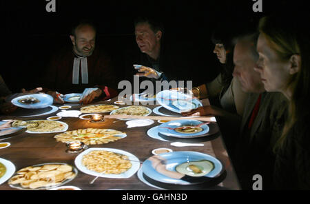 Artist Terry Flaxton (centre right) enjoys a virtual meal with diners at Winchester Cathedral including Rev Canon Roly Riem (centre left). The interactive piece entitled In Other People's Skins features a projection from above of people from various different cultures enjoying a meal together. Stock Photo