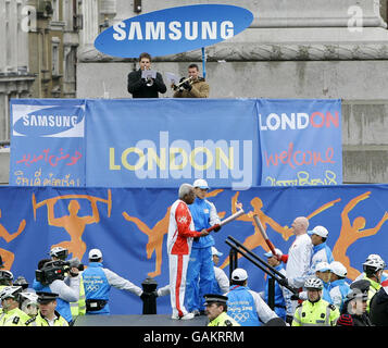 News reader Sir Trevor McDonald (left, centre) lights the Olympic torch held also by Chelsea Football Club Chief Executive Peter Kenyon at Trafalgar Square, London. Stock Photo