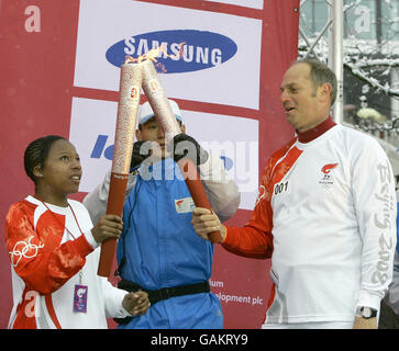 Olympic Gold medallist Sir Steve Redgrave (right) lights the Olympic torch held by Brent resident Cheyenne Green, 16, at Arena Square, Wembley, London. Stock Photo