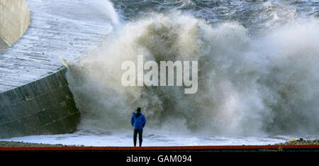 One man watches the waves crash against the walls of the historic Cobb at Lyme Regis in Dorset as high winds and spring tides batter the coast of England. Stock Photo