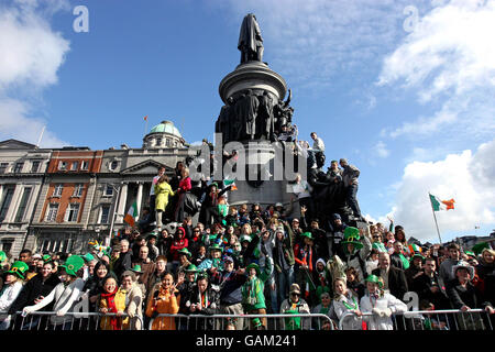 Revellers climb on to Dublin's famous Daniel O'Connell statue to get a better view of the annual St. Patricks Day Parade. Stock Photo