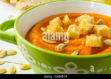 Pumpkin squash vegetable soup with croutons and pumpkin seeds in a green bowl on white wooden background, close up Stock Photo