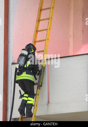 Firefighter with oxygen cylinder climbing a wooden ladder to put out the fire Stock Photo
