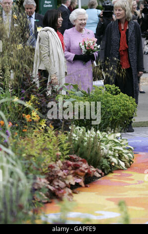 Queen Elizabeth II (centre) is shown the show garden 'From Life to Life, A garden for George', designed to celebrate the life of former Beatle George Harrison, his music and philosophy by designer Yvonne Innes (right) and Olivia Harrison, widow of George Harrison (left), during her visit at the Chelsea Flower Show in London. Stock Photo