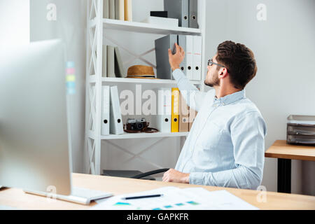 Handsome young businessman taking folder with documents from shelf in office Stock Photo