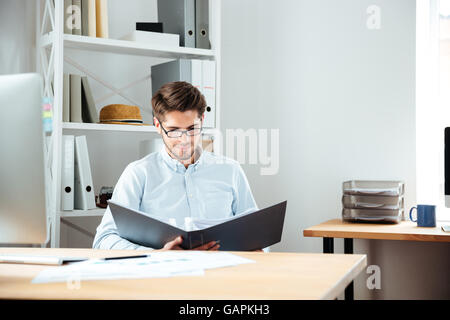 Concentrated young businessman working with documents in folder at workplace Stock Photo
