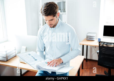 Concentrated young man working and holding folder with documents in office Stock Photo