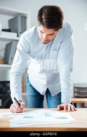 Serious young businessman staning and writing on the table in office Stock Photo