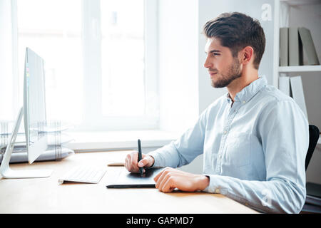 Handsome focused young man designer working using computer and graphic tablet in office Stock Photo