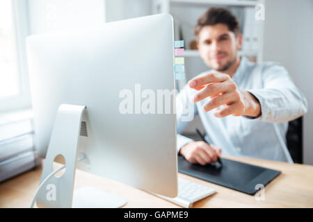 Closeup of young man designer putting stickers on monitor of comuter and using graphic tablet in office Stock Photo