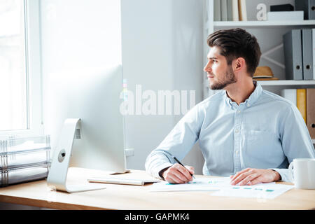 Pensive handsome bearded businessman sitting with laptop at office Stock Photo
