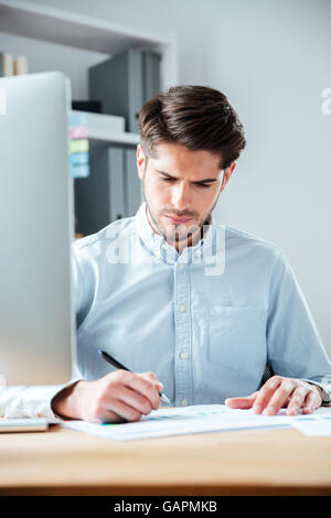 Confident young businessman sitting at the table and signing document in office Stock Photo