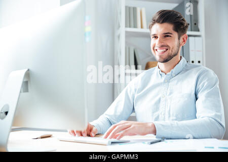 Smiling young happy businessman using laptop computer in office Stock Photo