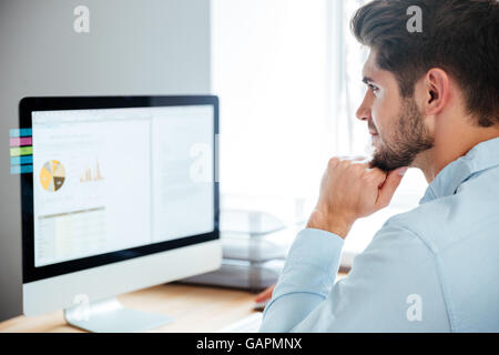 Side view of a young confident handsome businessman working on laptop in office Stock Photo