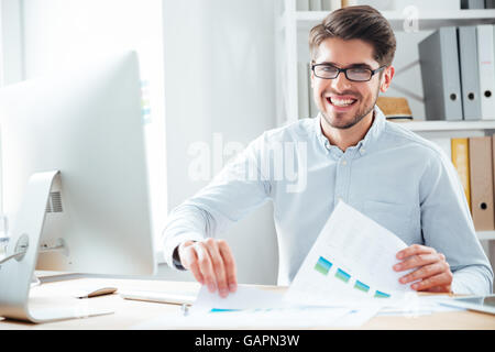 Smiling handsome young businessman working with documents and pc computer in office Stock Photo