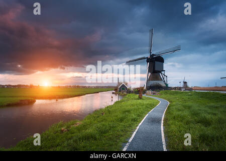 Landscape with traditional dutch windmills and path near the water canals. Clouds at colorful sunset in spring. Kinderdijk, Neth Stock Photo