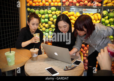 Two young Chinese women look at the work the third one did on the her laptop, one is even trying to help, smartphones are seen. Stock Photo