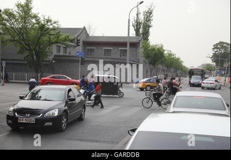 Scooters, tricycle trucks, bicycles and pedestrians cross the intersection all go through cars traveling, turning or stopping. Beijing, China. Stock Photo