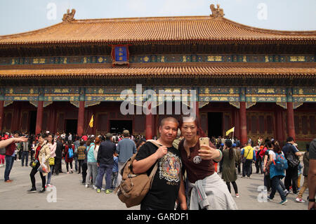 Woman uses a smartphone to take a selfie of her and her man in front of the Hall of Supreme Harmony, many tourists are around. Stock Photo