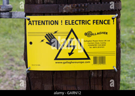 A sign warning of and electric fence surrounding a field of sheep "ATTENTION! ELECTRIC FENCE! Stock Photo