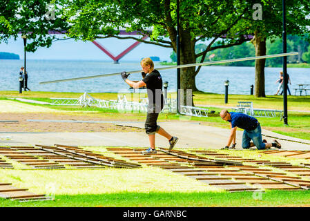 Motala, Sweden - June 21, 2016: Young adult workers clean up after an event in the park. One person is carrying long planks over Stock Photo