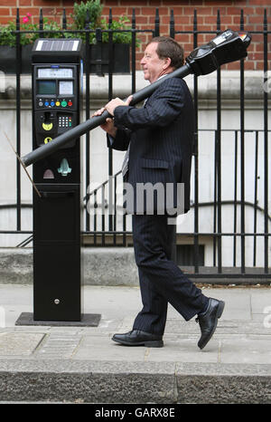 Robert Barnes, head of Parkeon, who manufacture London's parking meters, carries an original 1958 Duncan Single Space Parking Meter past a modern Strada Rapide meter in Grosvenor Square, London. Stock Photo